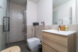 A modern bathroom with a glass shower enclosure, a toilet, a sink with wooden vanity, and a mirror.