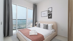 A modern bedroom with a large bed, grey curtains, and a city view through floor-to-ceiling windows.