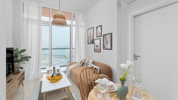A modern living room with a sofa, a dining table, and a view of the sea.
