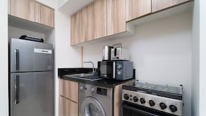 A compact kitchen with a stainless steel refrigerator, a washing machine, a microwave, and a gas stove.