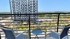 A balcony with two chairs and a small table, overlooking a parking area and a tall building.