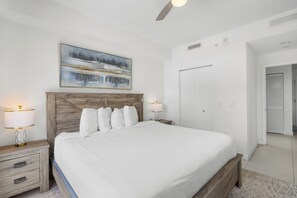Ein Schlafzimmer mit einem hölzernen Kopfteil, einem großen Bett, zwei Nachttischlampen, einem Gemälde über dem Bett und einer Tür rechts.