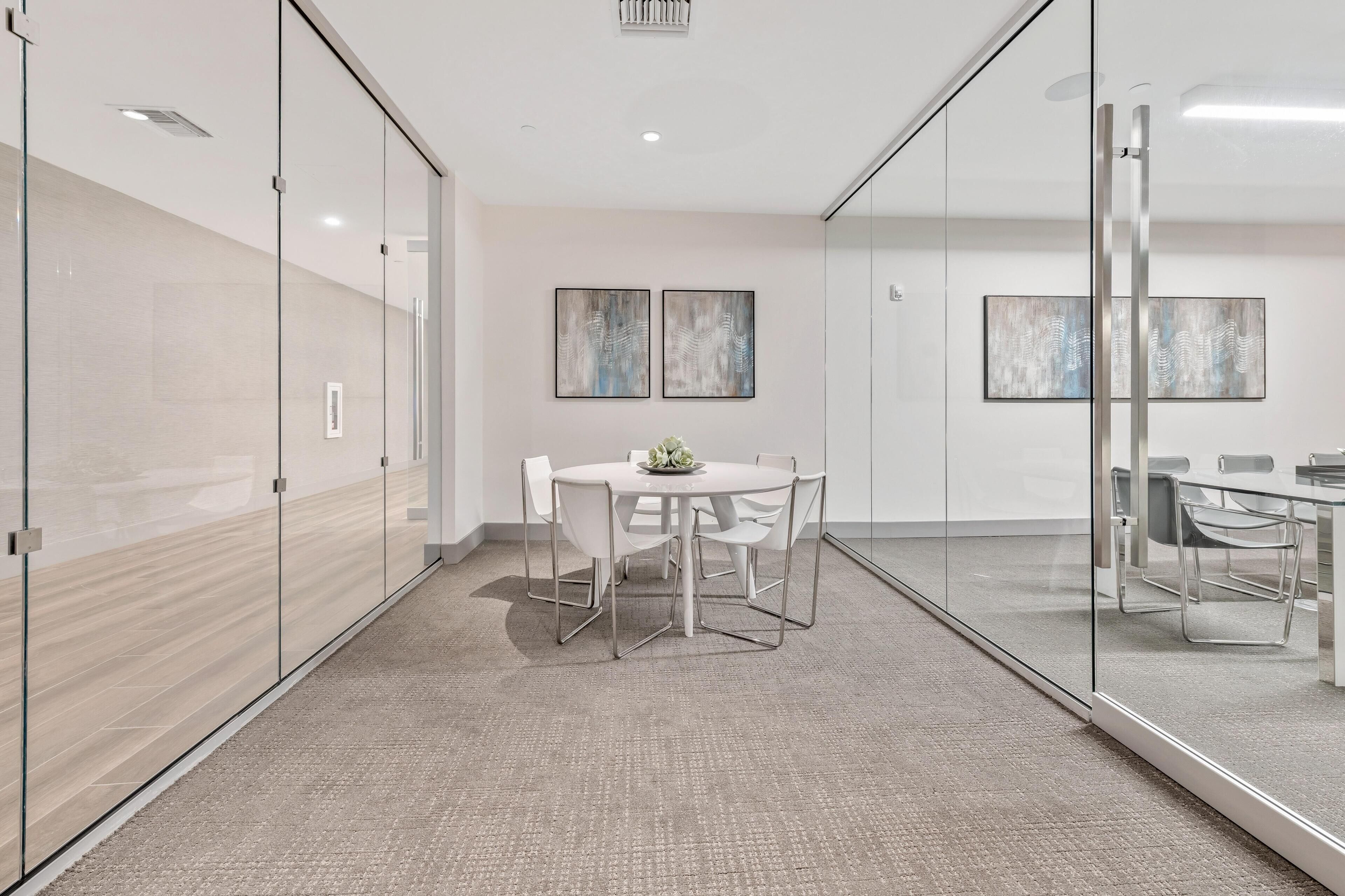 A modern conference room with glass walls, a round table with chairs, and two abstract paintings on the wall.