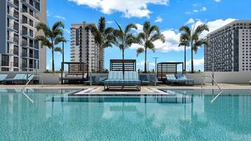 A swimming pool with lounge chairs and palm trees, surrounded by high-rise buildings.