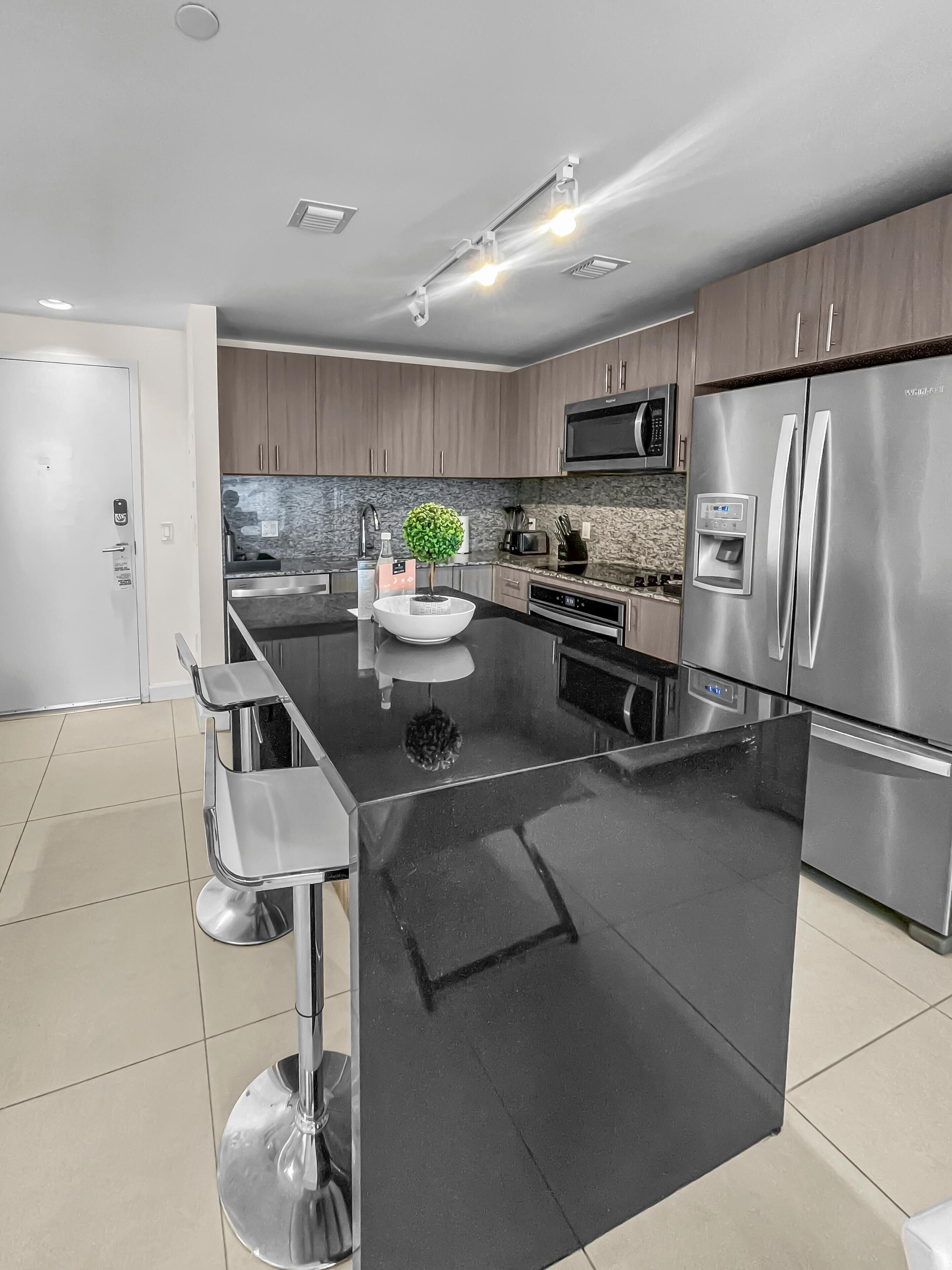 A modern kitchen with a central island, stainless steel appliances, and a stone backsplash.