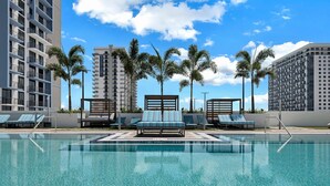 A swimming pool with lounge chairs and palm trees, surrounded by high-rise buildings. - Relaxing Doral Retreat: 2BR Charm (Doral)
