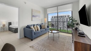 A modern living room with a sofa, coffee table, and a large window with a view of a building. - Modern Comfort: Doral 2BR Haven (Doral)