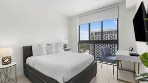 A modern hotel room with a large bed, a desk, a chair, and a large window offering a city view. - Modern Comfort: Doral 2BR Haven (Doral)