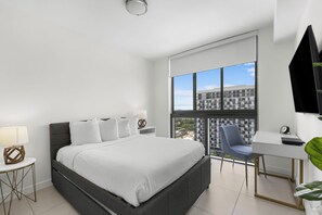 A modern hotel room with a large bed, a desk, a chair, and a large window offering a city view.
