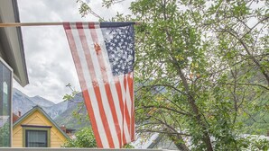 A balcony with two black chairs, a small wooden bench, and an American flag. - Downtown Dahl Haus: 2 bed/2 bath (Telluride)