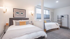 A hotel room with two beds, a wall-mounted artwork, a standing fan, and a window with blinds. - Downtown Dahl Haus: 2 bed/2 bath (Telluride)