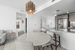 A modern kitchen with a stainless steel refrigerator, a dining area with a round table and chairs, and a hanging light fixture.