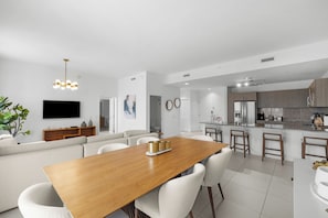 Una sala de estar moderna con una mesa de comedor de madera, sofás blancos y un televisor montado en la pared.