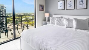 A modern bedroom with a large bed, a nightstand, and a view of a balcony with outdoor furniture. - Serene Doral Getaway: Kitchen Delight (Doral)