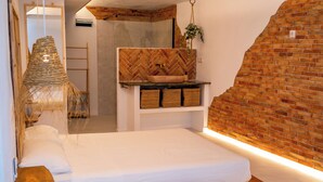 Une chambre avec un lit en bois, un mur en briques disposées en motif chevrons, une plante suspendue et une petite étagère avec des paniers.