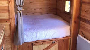 Une petite pièce en bois, aménagée comme une cabane, avec un lit simple, une fenêtre et un radiateur.