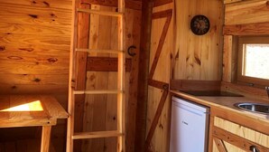L’intérieur de cette cabane en bois comprend une chambre à coucher située en mezzanine, une cuisine avec un évier et un lave-vaisselle Bosch, ainsi qu’une échelle en bois menant à la mezzanine.