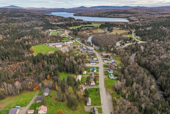 An aerial view of a small town with a river running through it, surrounded by dense forests and a lake in the background. - Spacious, family friendly 5-bedroom home in Pittsburg village with trail access. (Pittsburg)