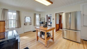 A modern kitchen with wooden flooring, a stainless steel refrigerator, and a wooden table with kitchen appliances. - Spacious, family friendly 5-bedroom home in Pittsburg village with trail access. (Pittsburg)