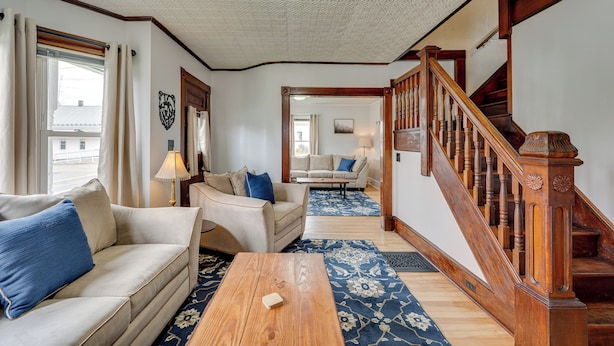 A spacious living room with a wooden staircase, a sofa, a coffee table, and a patterned rug. - Spacious, family friendly 5-bedroom home in Pittsburg village with trail access. (Pittsburg)