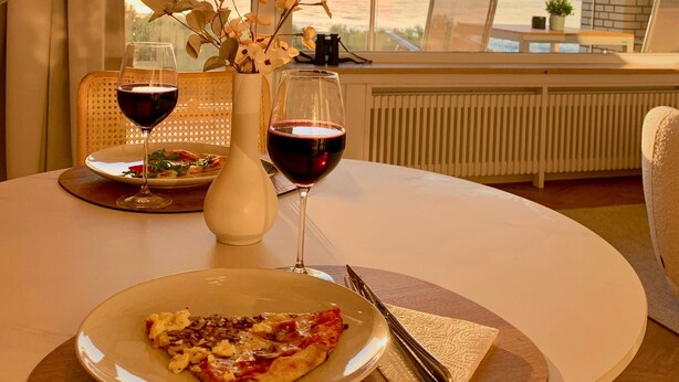 Ein Esstisch mit einer Pizzaplatte, zwei Weingläsern und einer Blumenvase.