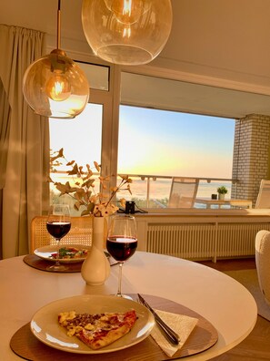 Une table à manger avec une assiette de pizza, deux verres à vin et un vase rempli de fleurs.