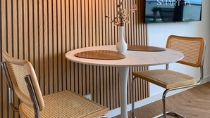 Ein modernes Interieur mit einem runden Tisch, zwei Korbstühlen, einer weißen Vase mit Blumen und einem an der Wand befestigten Fernseher, der "55 ZOLL SMART-TV" zeigt.