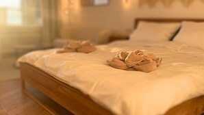 Ein ordentlich bezogenes Bett mit Holzrahmen und weißer Bettwäsche, ein Paar Handtücher auf dem Bett, und ein Fenster mit Vorhängen im Hintergrund.