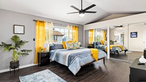 A bedroom with a bed, bedside tables, a ceiling fan, a large mirror, and a potted plant. - Fun-Filled Family Vacay Home! 15 min to Disney! (Fullerton)