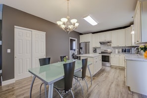 A modern kitchen with white cabinets, a glass dining table, and a chandelier. - Beautiful 4-bedroom house Central to St. Louis and St. Charles (St. Louis)