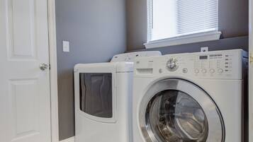A laundry room with two white front-loading washing machines and a window above them.