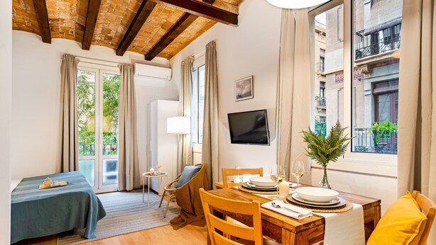A room with a bed, a dining table set for two, a TV, and a window with a view of buildings. - BARCELONETA BEACH STUDIO 11 (Barcelona)