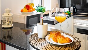 A breakfast setting with a croissant on a plate, a glass of orange juice, a bowl of fruit, and a white mug on a kitchen counter. - BARCELONETA BEACH STUDIO 11 (Barcelona)