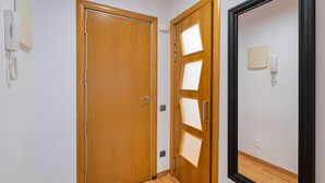 A wooden door with a phone on the wall to the left, a mirror with a black frame, and a light switch on the wall to the right. - VILLA DE GRACIA APARTMENT (Barcelona)
