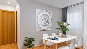 A modern dining area with a white table, white chairs, a large abstract painting, and two potted plants. - VILLA DE GRACIA APARTMENT (Barcelona)