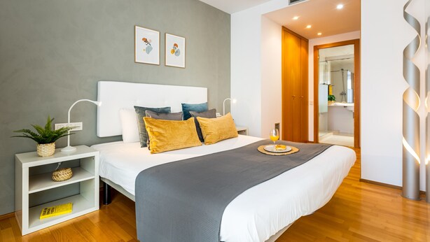 Ein modernes Schlafzimmer mit einem großen Bett, Nachttischen, einer Lampe, einer Pflanze und Kunstwerken an der Wand.