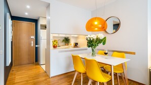 Eine moderne Küche mit weißen Schränken, einer Holztür und einem Essbereich mit weißem Tisch und gelben Stühlen.