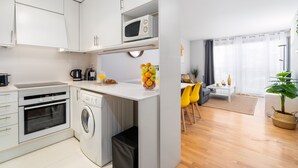 Eine kompakte Küche mit Mikrowelle, Backofen und Waschmaschine. Ein Essbereich mit einer Couch und Stühlen ist zu sehen.