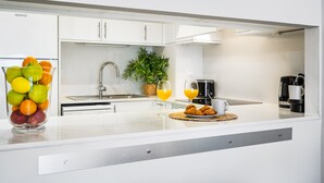 Eine moderne Küche mit weißen Schränken, einer Edelstahl-Spüle, einem Blumentopf, einer Obstschale und einer Kaffeemaschine.