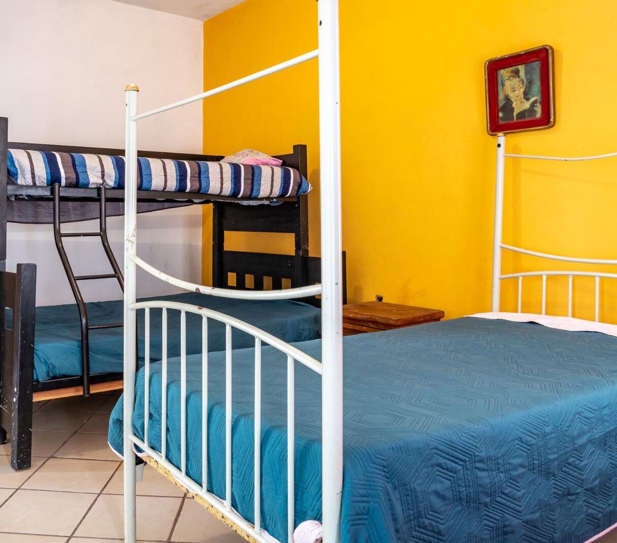 A room with bunk beds and a single bed, a wooden chair, and a small table.