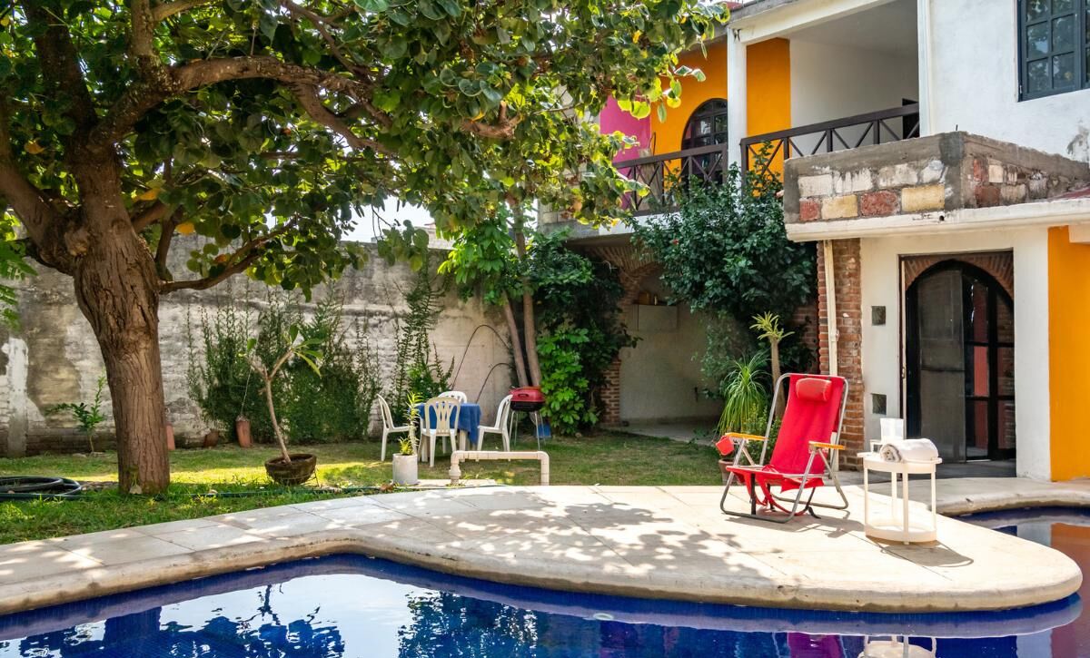 A swimming pool with lounge chairs, a tree, and a building with a balcony.
