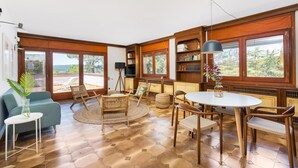A spacious living room with a large round table, comfortable seating, a bookshelf, and large windows offering a view of the outdoors. - Lodging Apartments Villa el Racó (Santpedor)