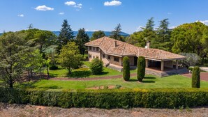 A large, single-story house with a tiled roof, surrounded by well-maintained gardens and trees. - Lodging Apartments Villa el Racó (Santpedor)