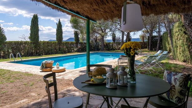 An outdoor pool area with a thatched roof, a table with a vase of flowers, and lounge chairs. - Lodging Apartments Villa el Racó (Santpedor)