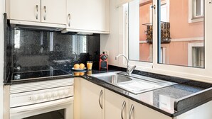 Eine moderne Küche mit weißen Schränken, einer schwarzen Arbeitsplatte, einer Edelstahlspüle und einem Fenster mit Blick auf ein Gebäude.
