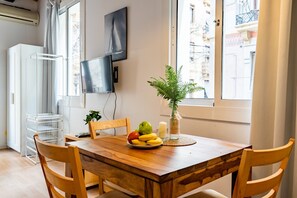 A dining area with a wooden table, chairs, a fruit bowl, a potted plant, and a TV on the wall.