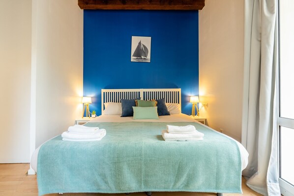 A neatly made bed with a teal bedspread, two white towels, and a framed picture on the headboard.