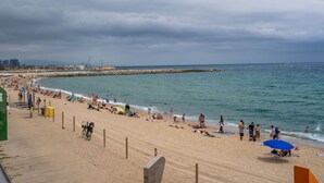 A beach with people sunbathing and swimming, a rocky breakwater, and a city skyline in the background. - BARCELONETA BEACH STUDIO 42 (Barcelona)