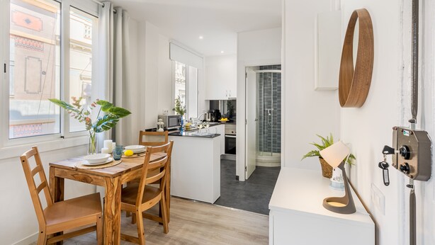A modern kitchen with a central island, white cabinetry, and a dining area with wooden chairs.