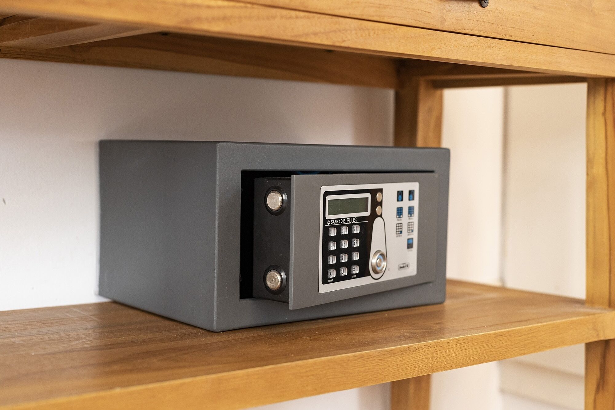 Een grijze kluis met een keypad en een digitaal scherm, bevestigd aan een houten plank.